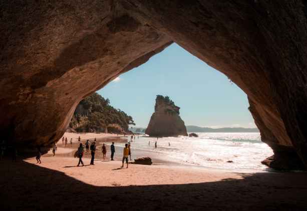people walking beside cave and body of water