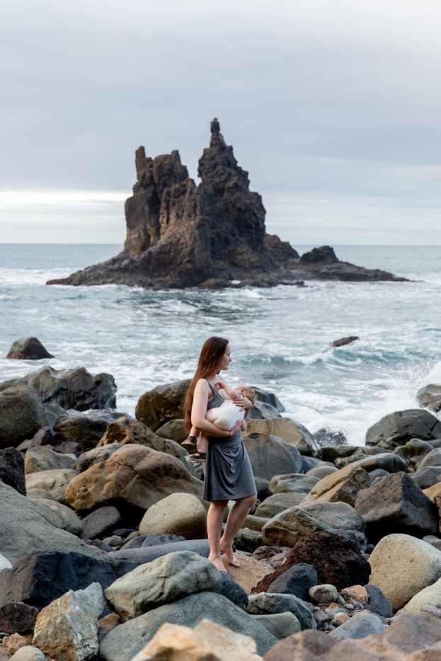young mother with little baby on hand while standing on rocky seashore