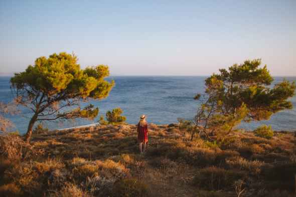 woman in red dress standing on a cliff near the sea