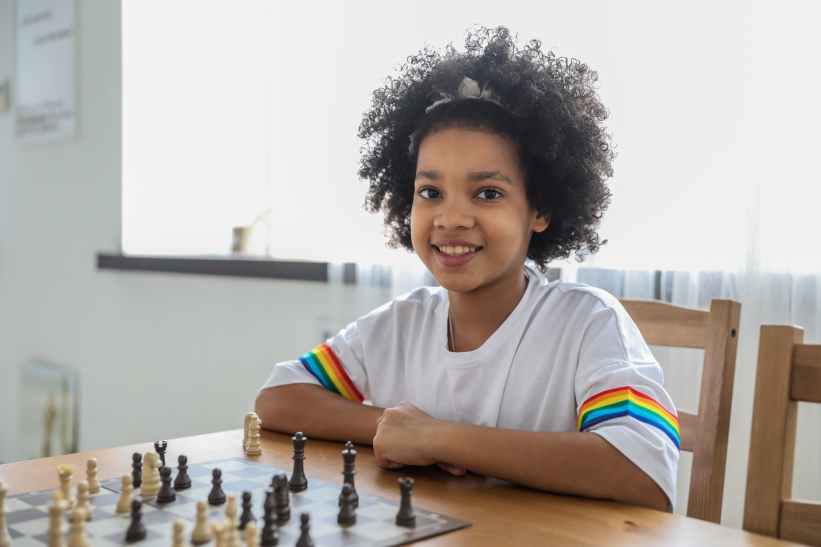 black girl playing chess at table in room